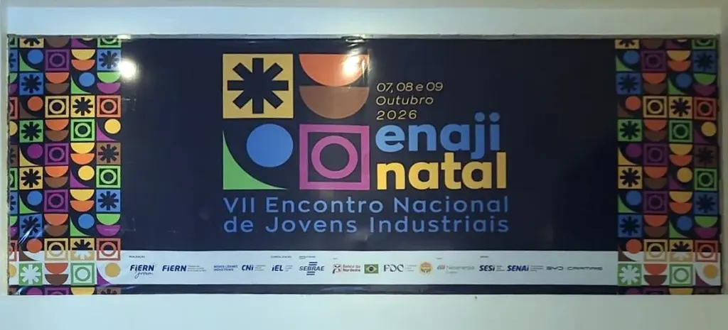 Banner do evento ENAJI Natal 2026 instalado em parede interna, com a arte colorida do encontro e os logotipos dos apoiadores
