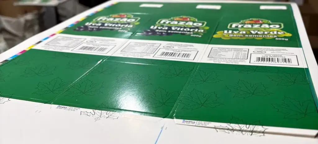 Folha impressa com cintas em cartão triplex C1S 190 g para embalagem de uva, com corte especial e colagem, empilhada na produção da iGráfica